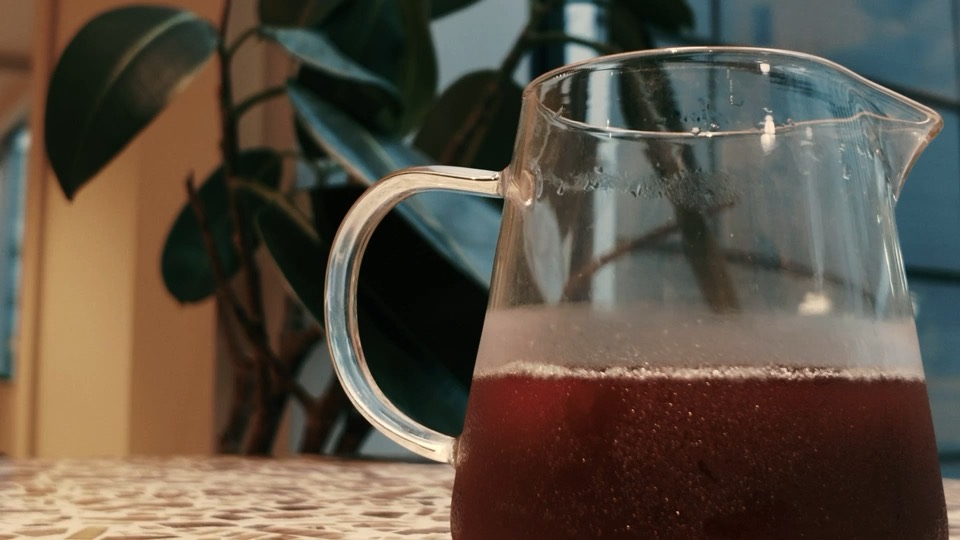 A glass carafe of filter coffee on a table, a rubber plant behind it.
